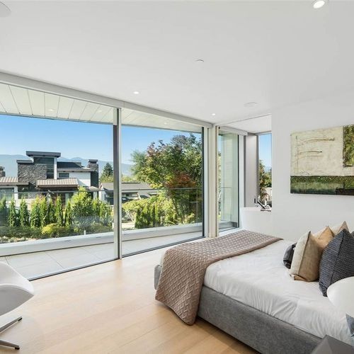 Modern bedroom with large floor-to-ceiling windows overlooking a landscaped view