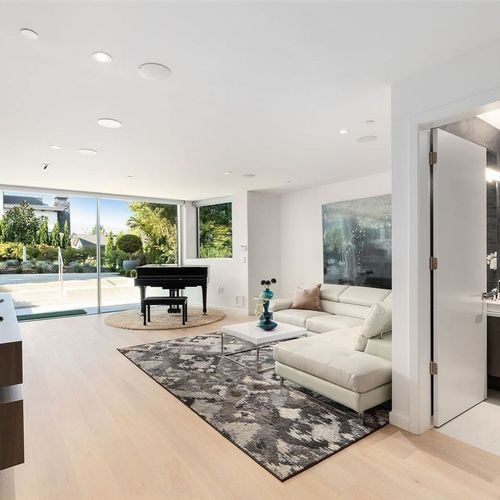 Bright modern living room with white sectional, black piano, and large sliding glass doors to a sunny patio