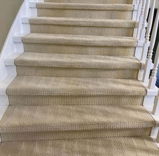 Beige carpeted staircase with white railings leading upward indoors