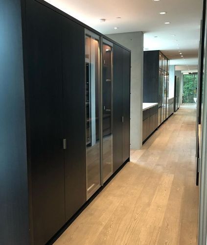 Modern hallway with dark cabinets, wood floor, and large windows at the far end