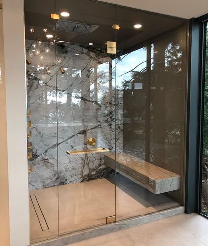 Glass phone booth with marble wall, wood bench, and small round table in a modern office hallway