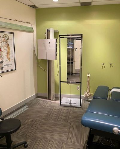Medical exam room with green walls, exam table, sink, mirror, and chair.