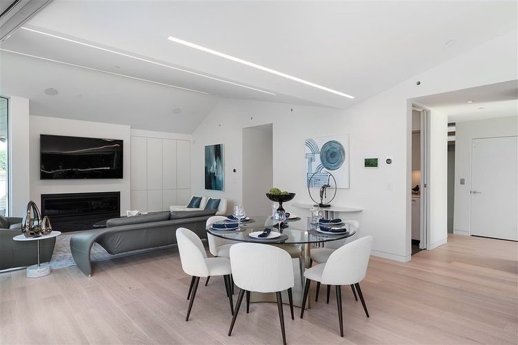 Bright modern living room and dining area with gray sectional, white chairs, and large wall TV