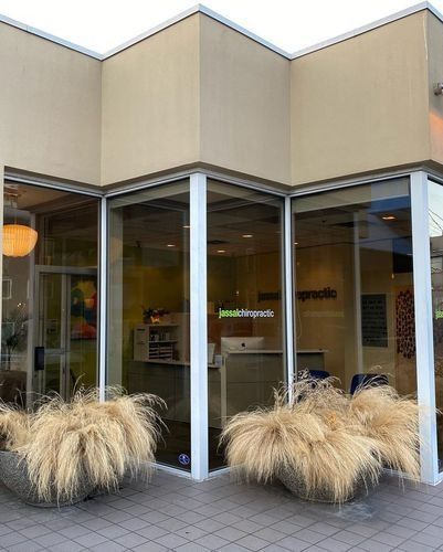 Corner storefront with large windows and tan facade, flanked by tall ornamental grasses in planters.