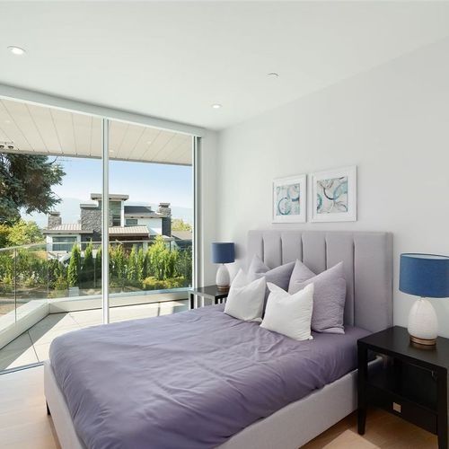 Bright bedroom with a gray bed, blue lamps, and floor-to-ceiling windows overlooking a patio and greenery
