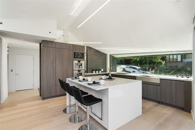 Modern white kitchen with island, barstools, wood cabinets, and large garden-view window