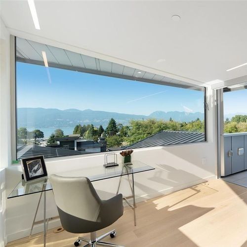 Modern home office with a glass desk, chair, and panoramic mountain view through large windows