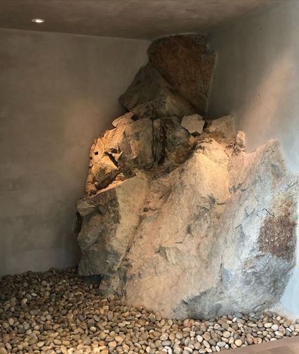Large boulder formation inside a gray enclosure, surrounded by a pebble-covered floor.