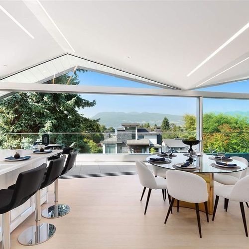 Modern dining terrace with white tables, black chairs, and mountain views through large open windows