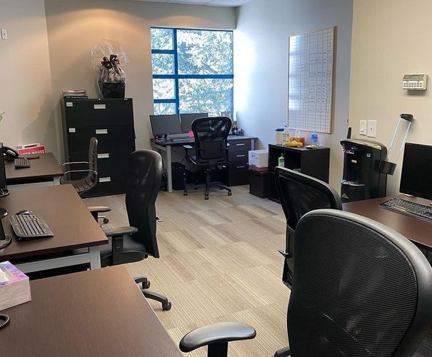 Empty office with desks, black chairs, filing cabinets, and a window letting in daylight.