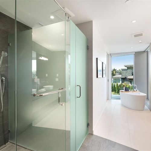 Modern bathroom with frosted glass shower, white tile, and freestanding tub by a window