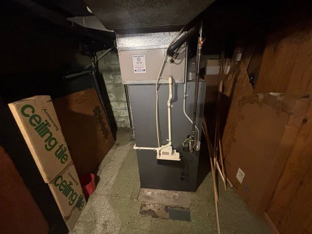 Gray metal HVAC/furnace unit with ductwork in a bare utility room