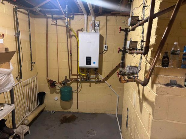 Two white wall-mounted boilers with copper pipes in a concrete basement utility room