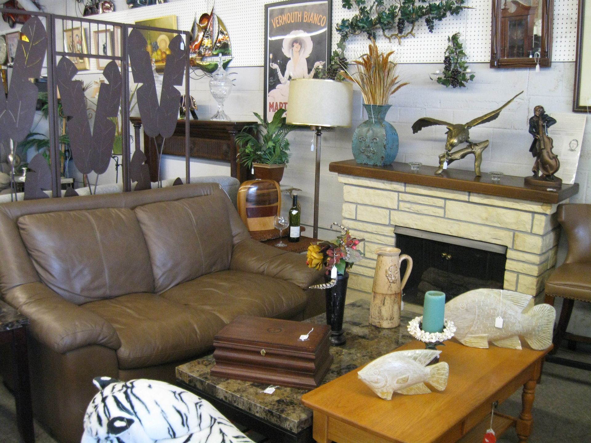 Living room with brown leather couch, fireplace, coffee table, and decorative shelves and plants