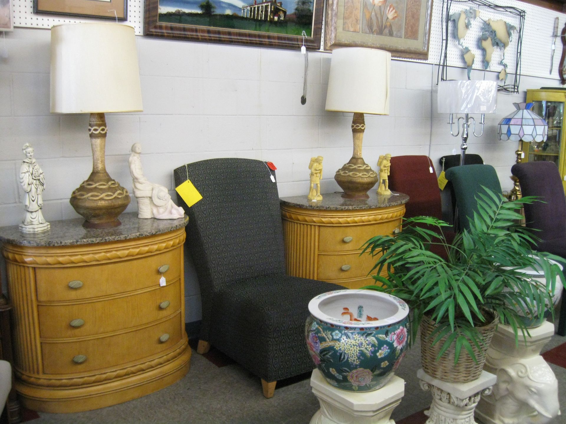 Furniture showroom with two gold lamps, dark chair, wooden tables, and potted plants