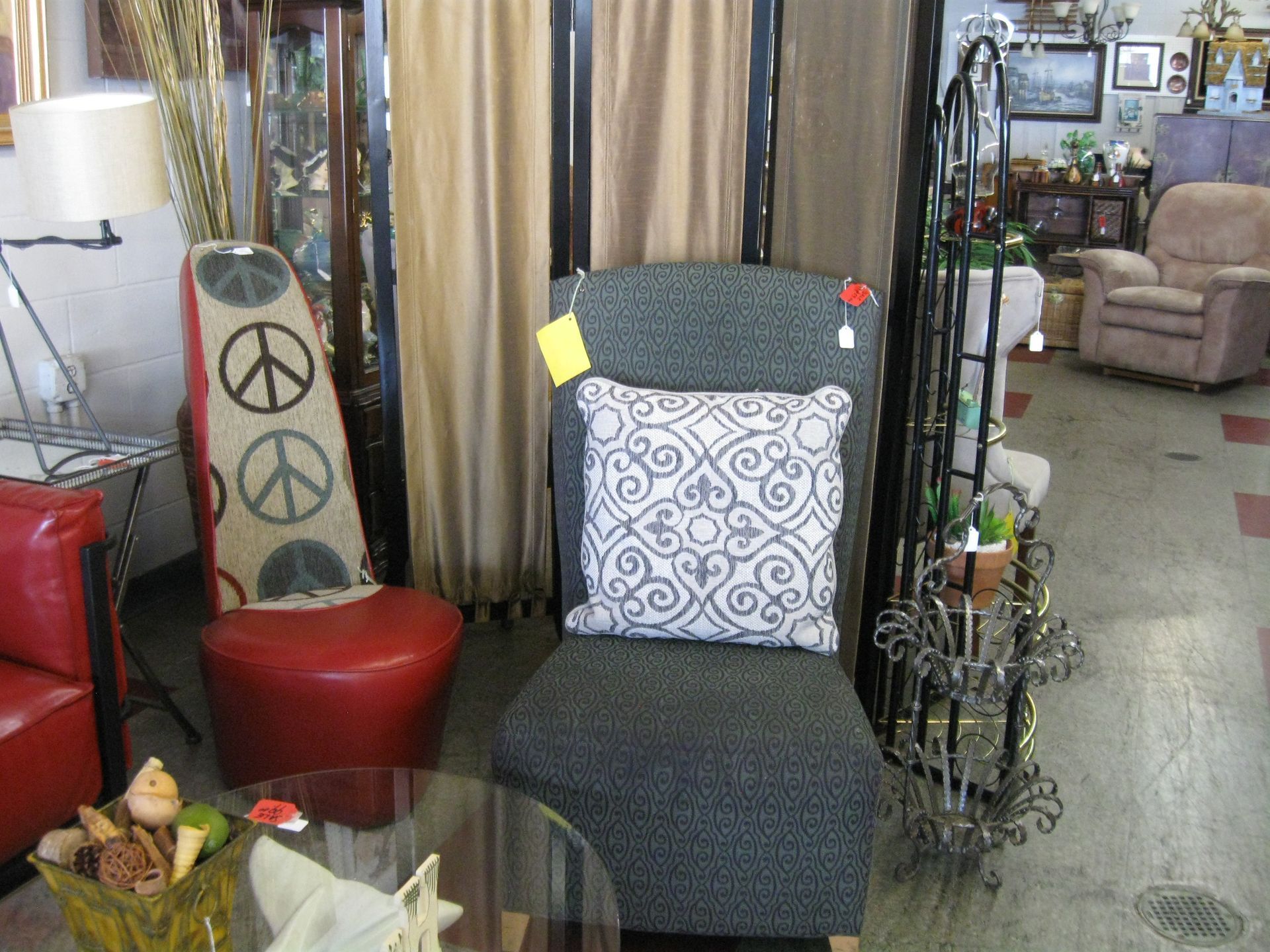 Furniture display with dark chair, peace sign decor, red stool, glass table, and cushions in a showroom