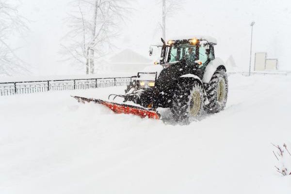 A tractor is plowing snow on a snowy road.