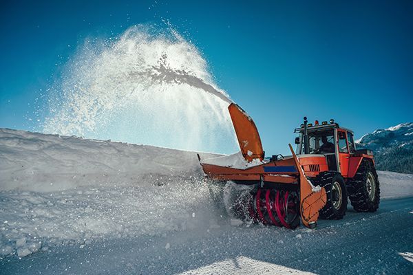 A snow blower is blowing snow from a tractor.