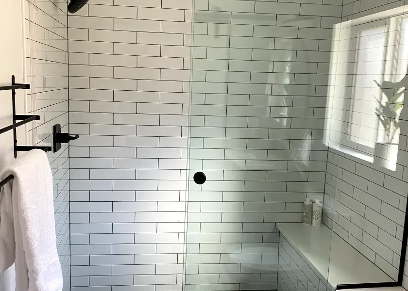 A bathroom with white brick walls and a walk in shower with a glass door.