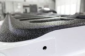 Black textured mat on a white metal surface, close-up with a small hole in the foreground.
