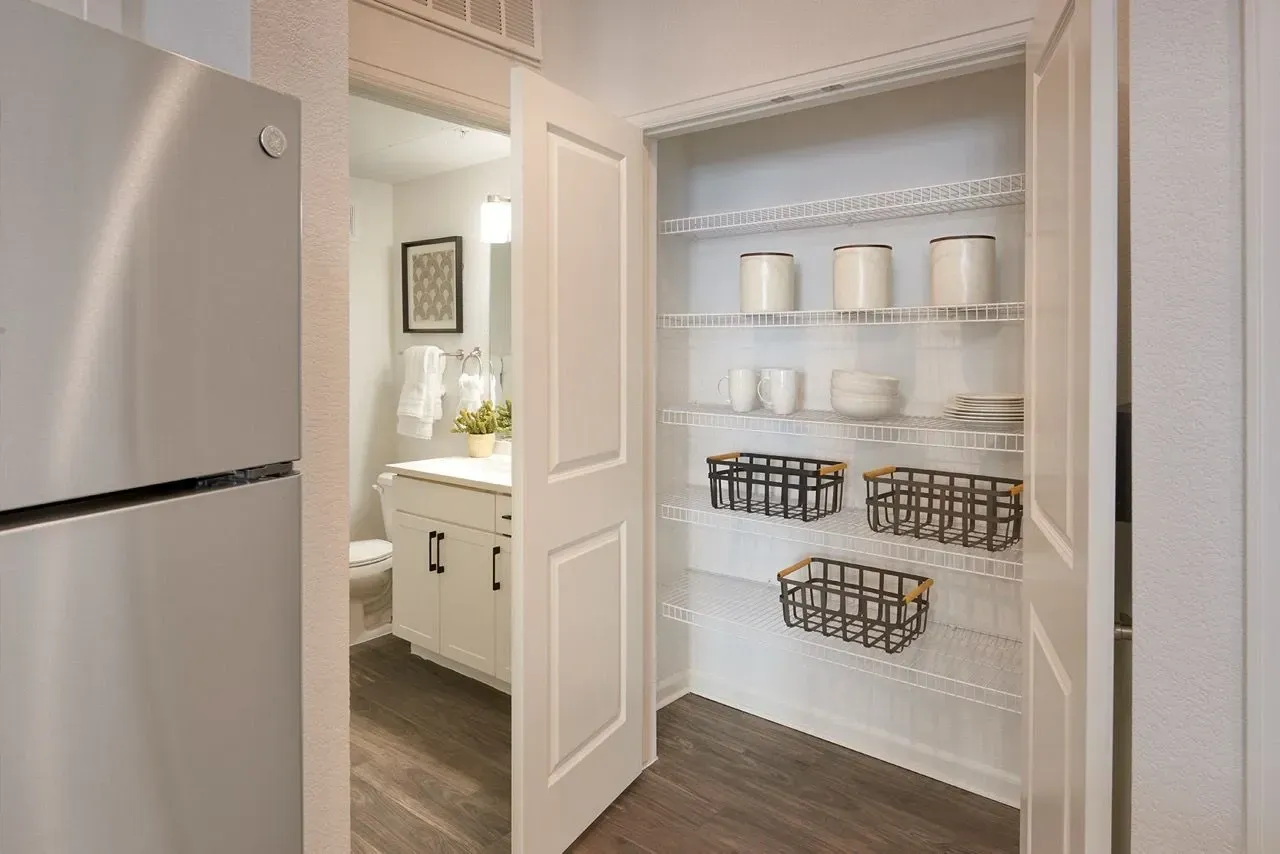 Spacious pantry with shelving and decorative baskets, adjacent to a bathroom.