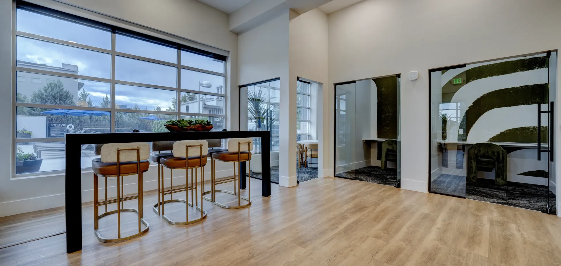 Modern communal lounge area with a high table, bar stools, and glass-enclosed rooms.