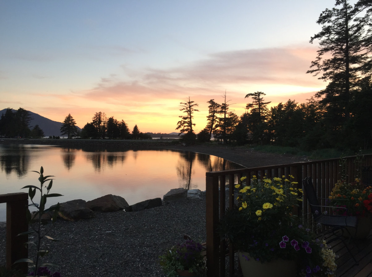 Sunset over a calm lakeside with silhouetted trees and a wooden deck in the foreground
