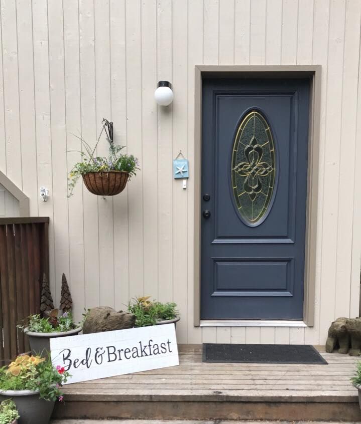 Bed and breakfast entrance with navy door, hanging flower baskets, and a white sign by the steps