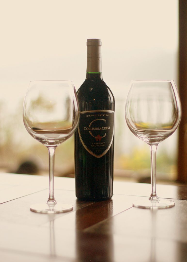 Wine bottle centered between two empty wine glasses on a table by a window.