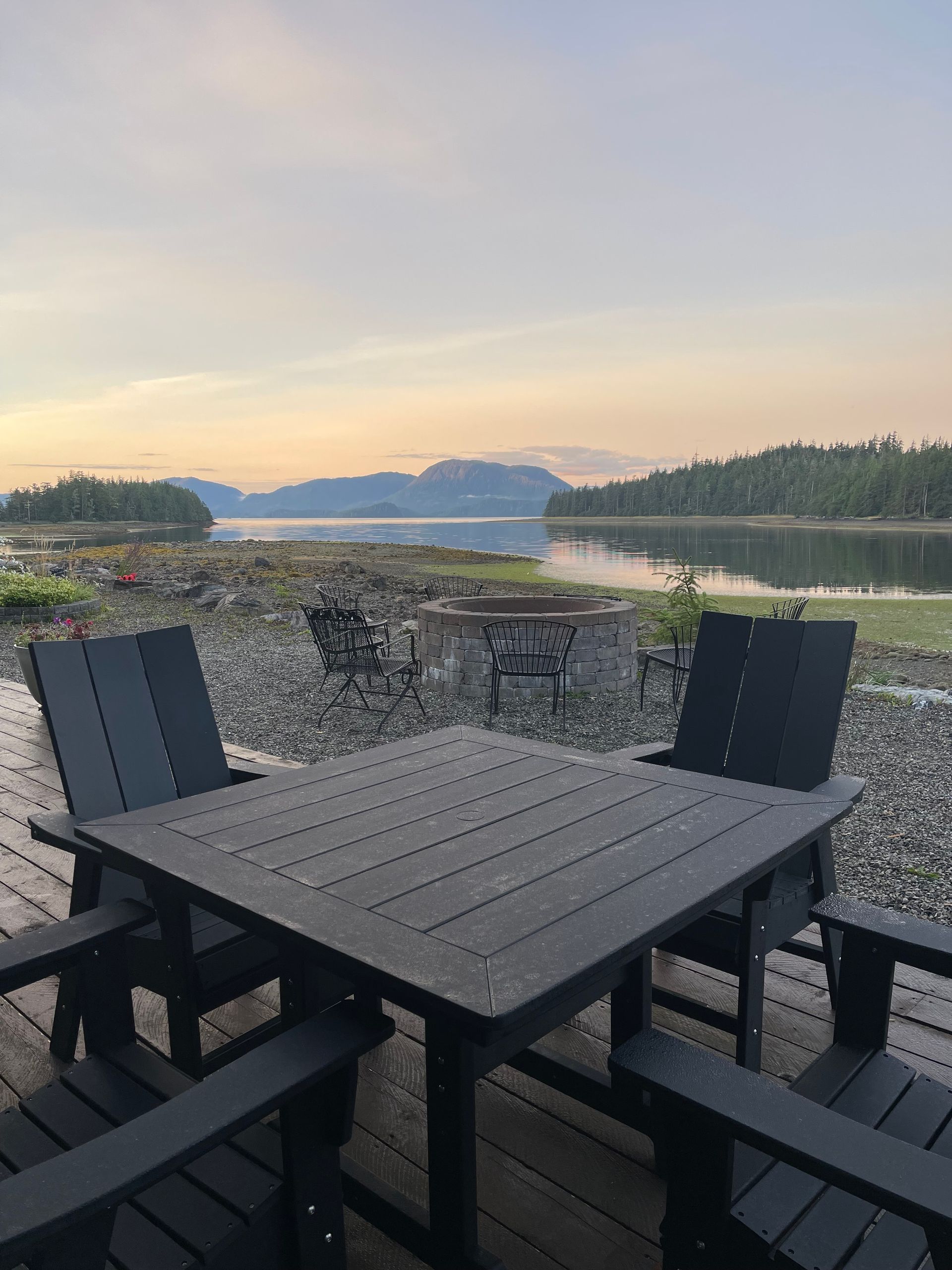 Patio table and chairs overlooking a calm river at sunset with mountains in the distance