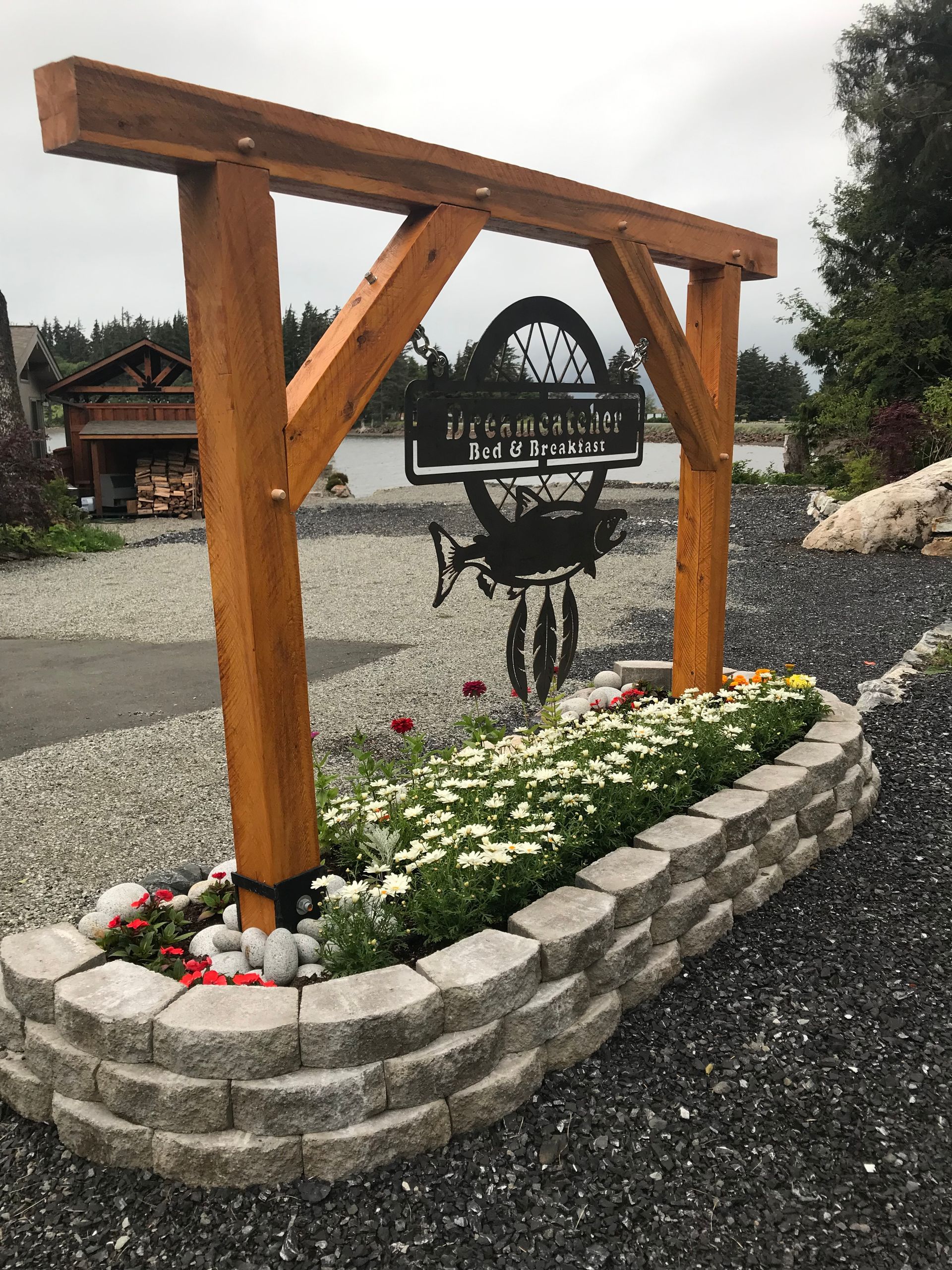Wooden garden arch over a stone flower bed with white blooms and hanging black planter