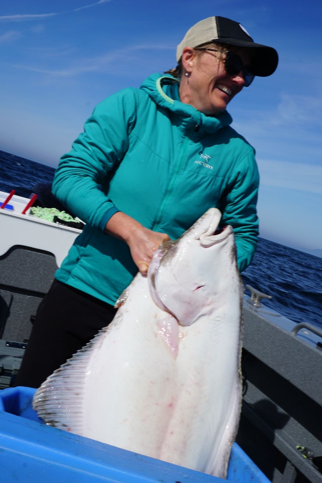 Smiling person on a boat holding a large white fish against a blue ocean backdrop