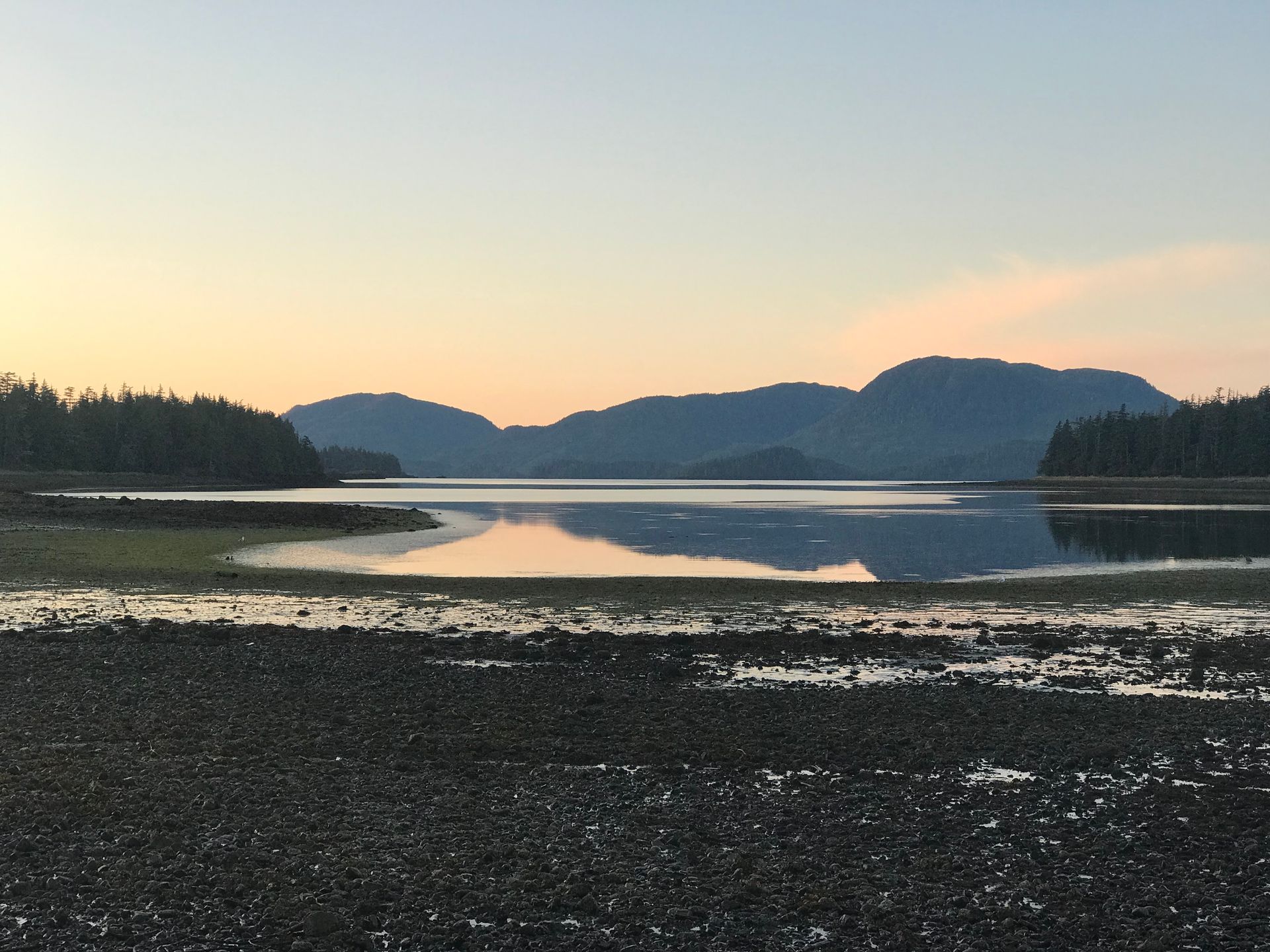 Sunset over a calm mountain lake with reflective water and dark forested shores