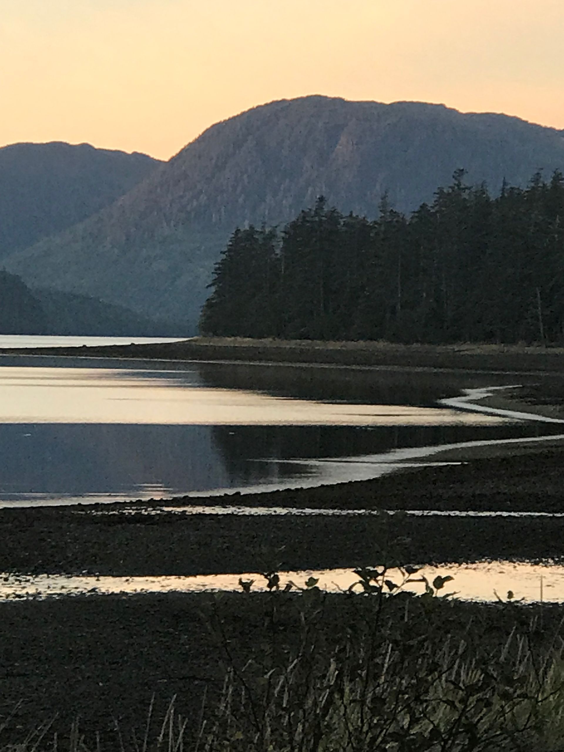 Serene lake at sunset with dark mountain silhouettes and a forested shoreline reflected in calm water