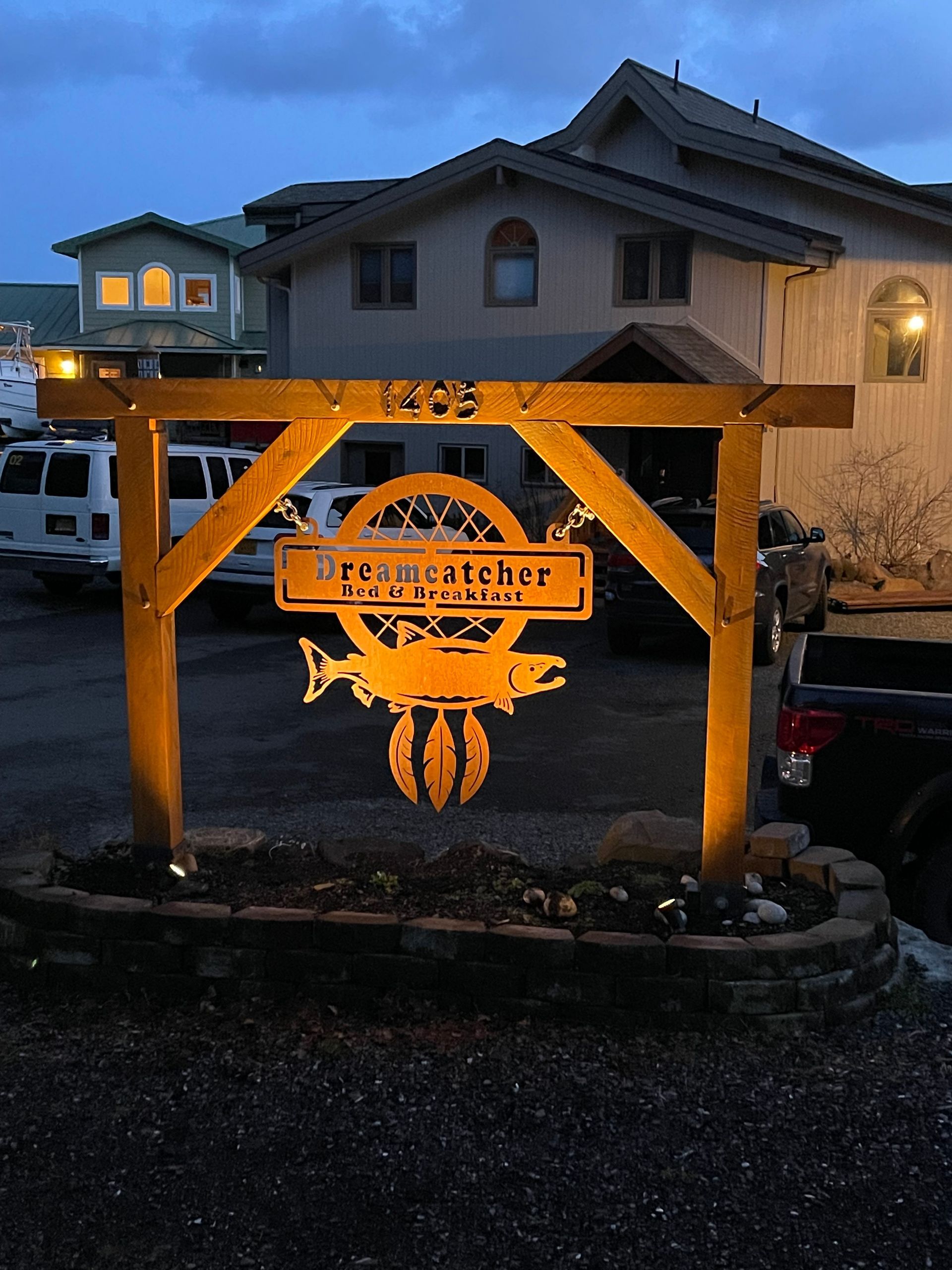 Lit wooden sign with glowing orange crab emblem in front of a house at dusk