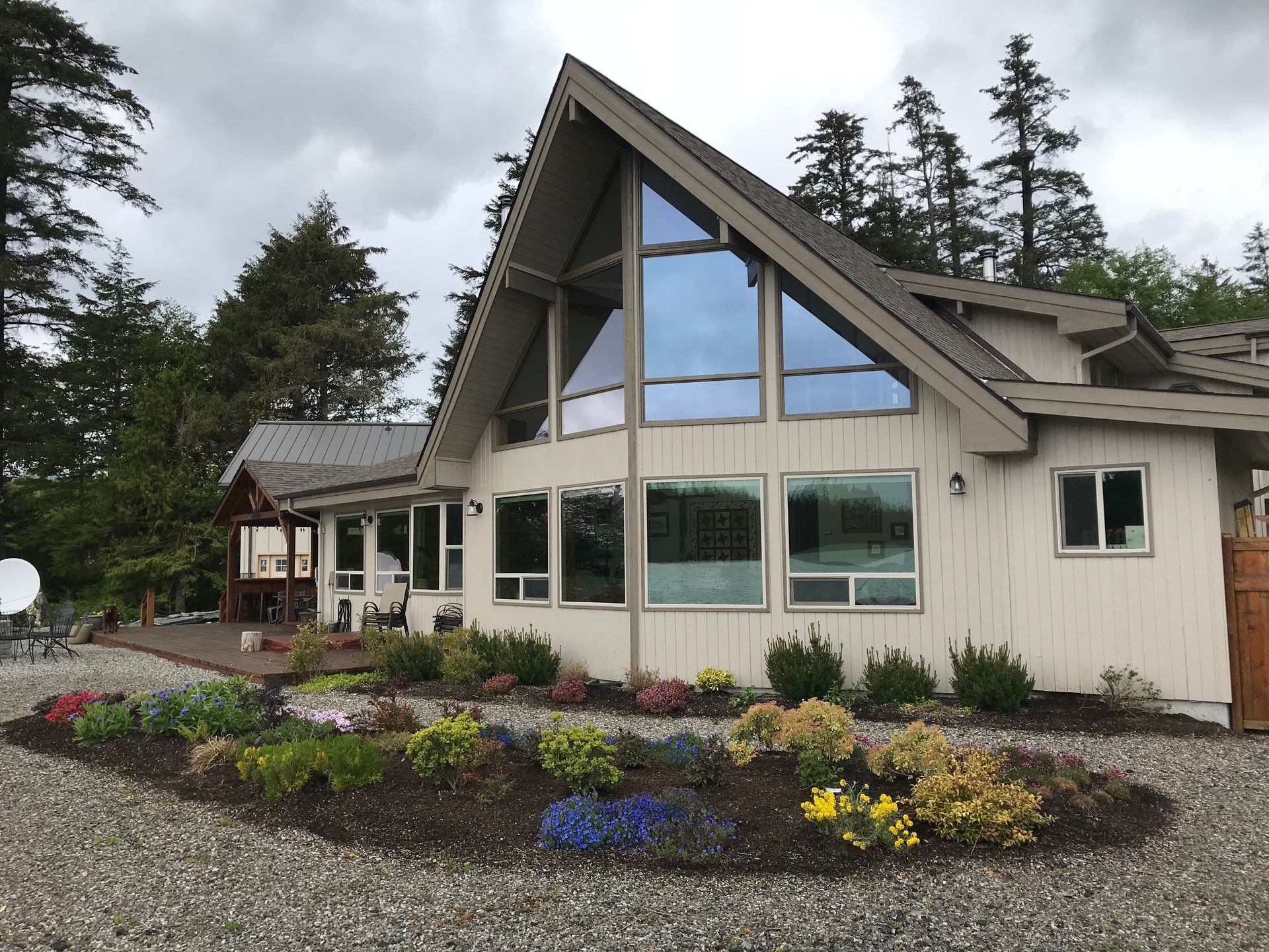 Modern house with steep roof, large windows, and a landscaped flower garden under cloudy skies