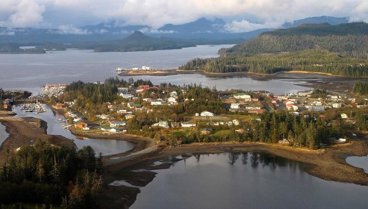 Coastal village on a lagoon with roads, houses, hills, and clouds under a bright sky