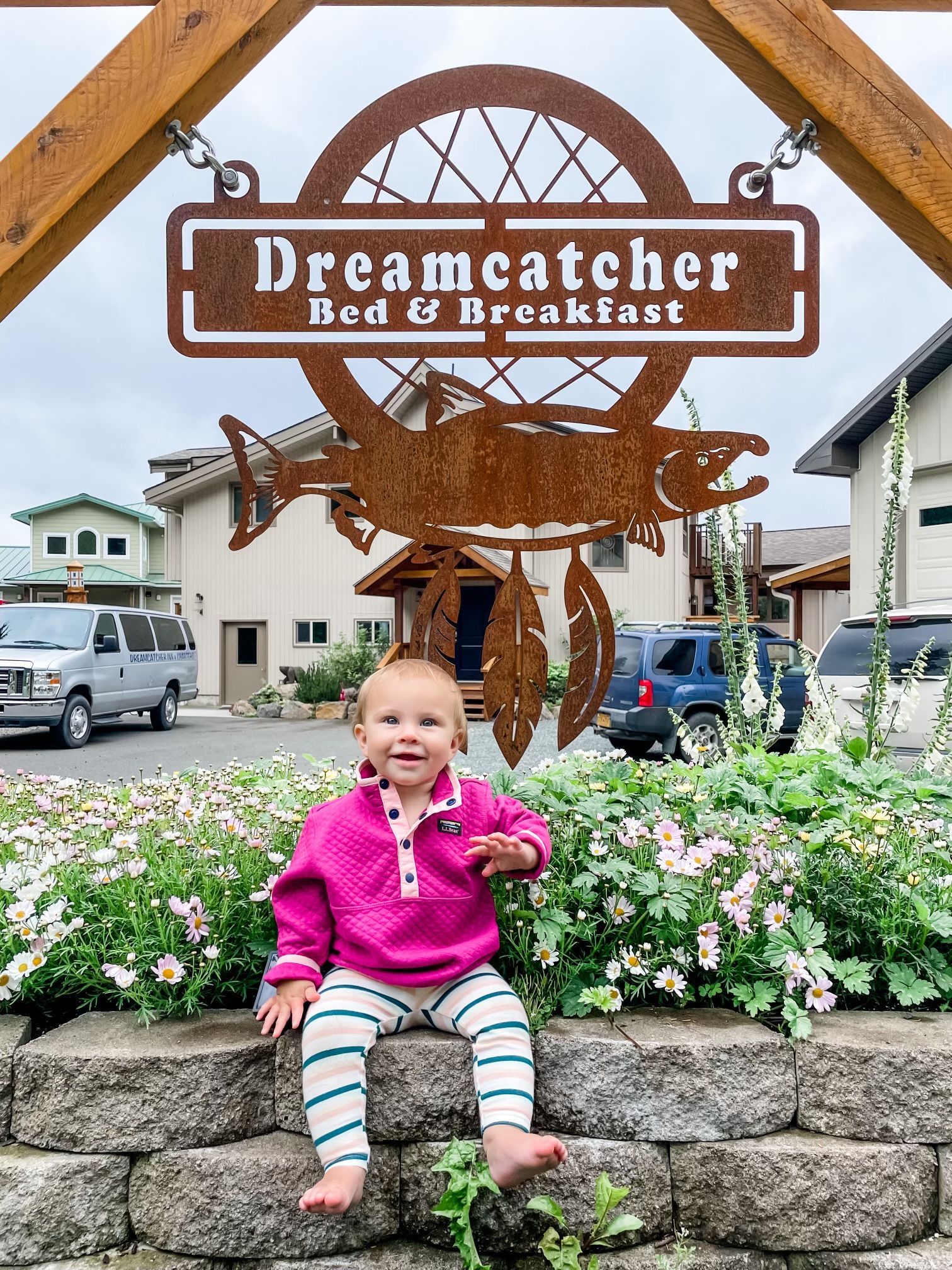 Toddler sitting on stone steps in front of Dreamcatcher Bed & Breakfast sign and floral garden