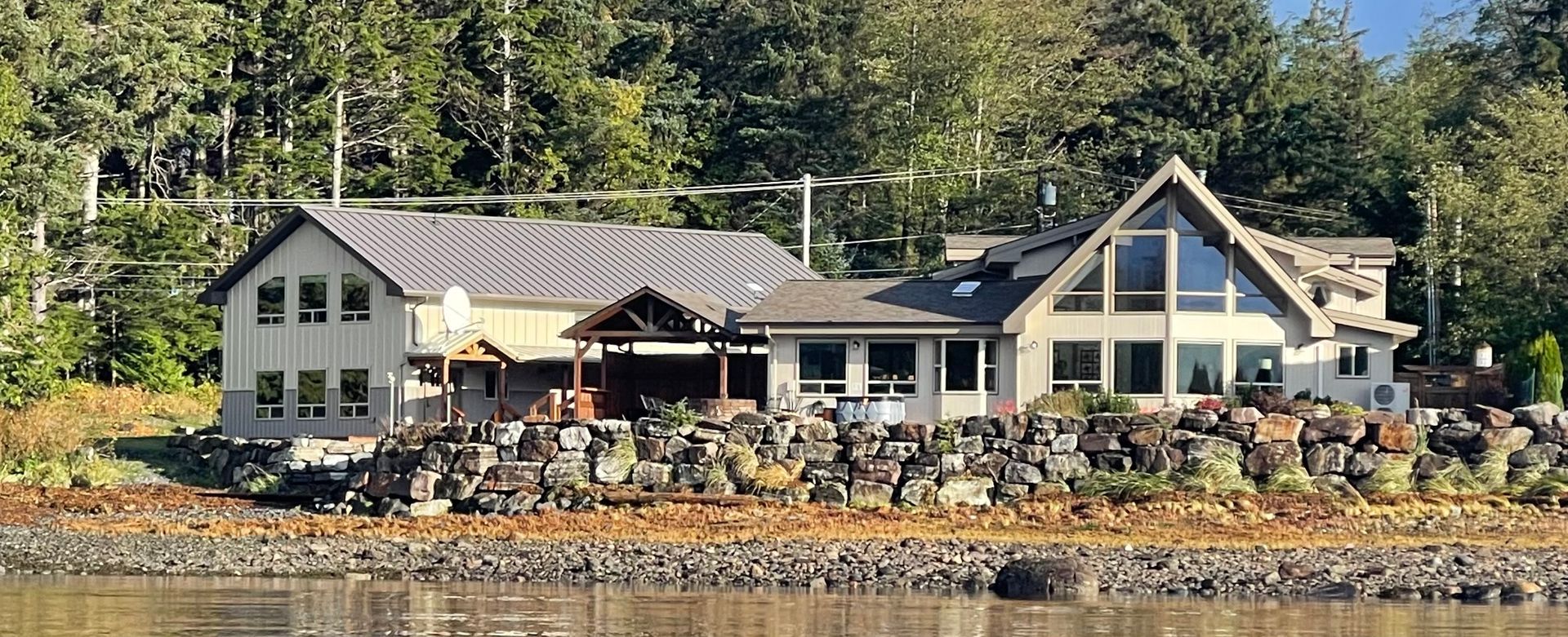 Lakeside white house and boathouse with docked rowboats, set against trees and water