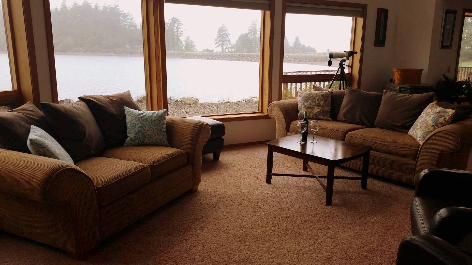 Cozy living room with two sofas, coffee table, and large windows overlooking a lake.