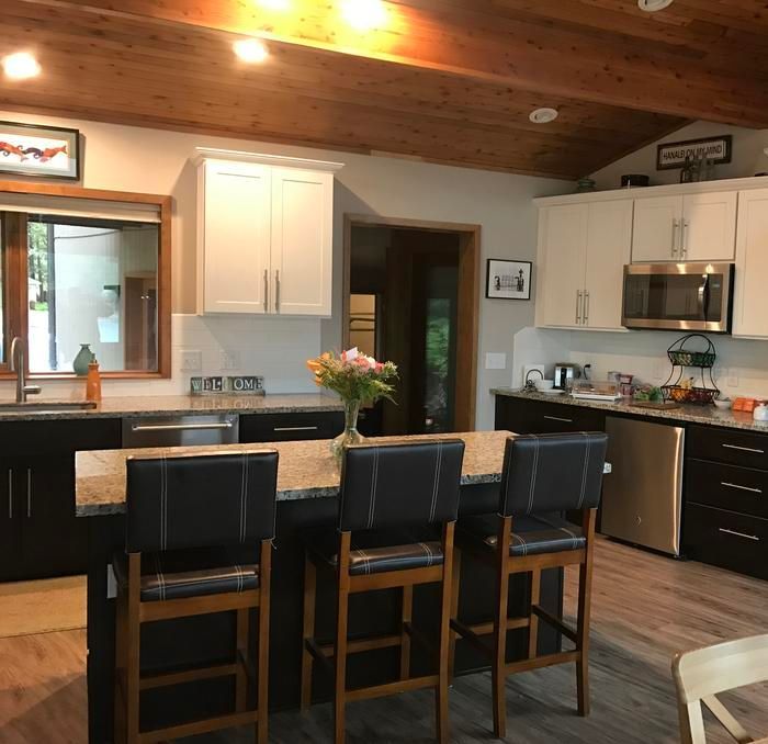 Modern kitchen with island seating, white cabinets, black countertops, and wood ceiling with warm lighting