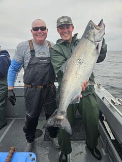 Two anglers on a boat holding a large silver salmon on a cloudy day