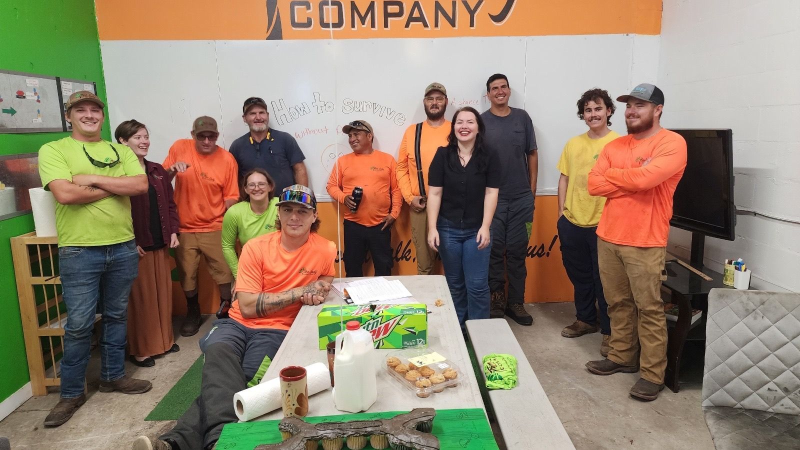 A group of people wearing work attire posing indoors in front of a company sign.