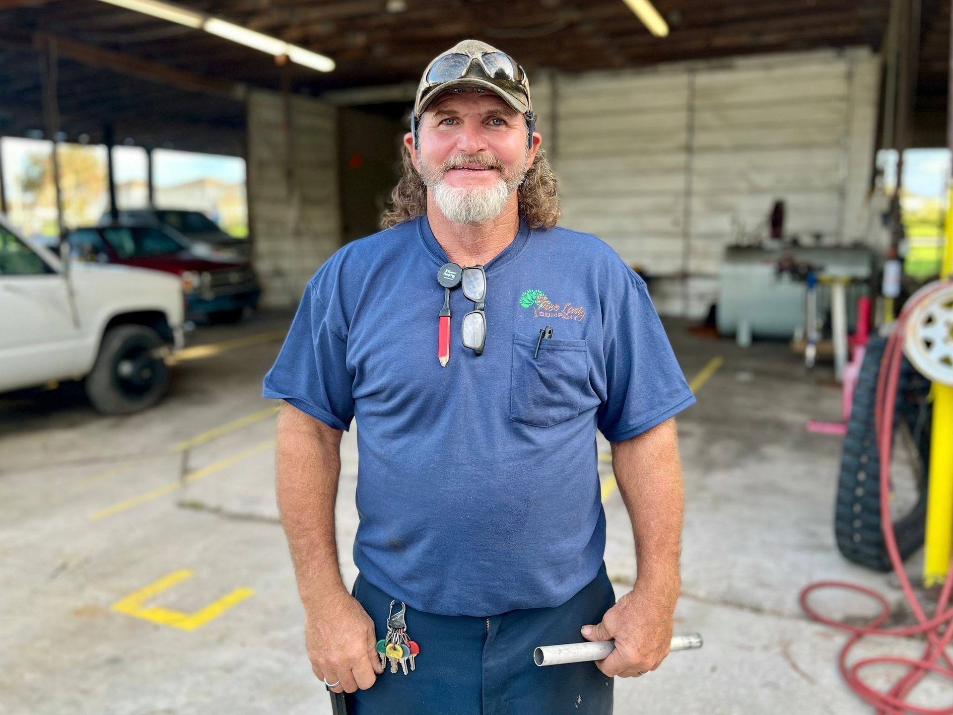 Man in blue shirt and camo hat stands in garage, holding a pipe wrench.