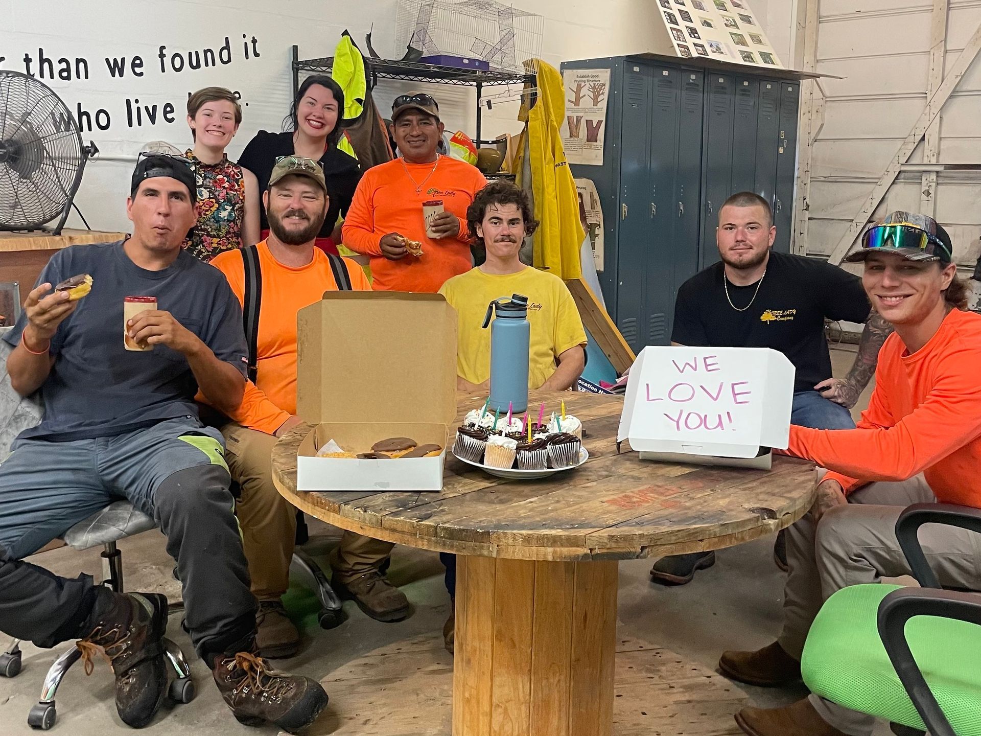 A group of people gather around a table with treats, holding a 