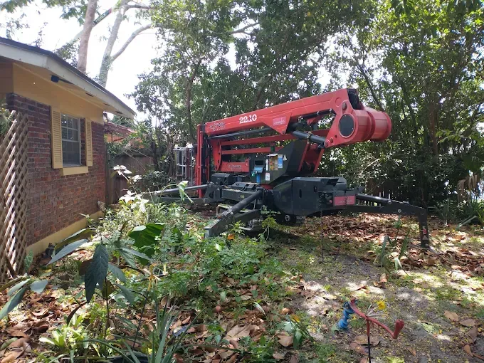 A red crane removing trees near a brick building.