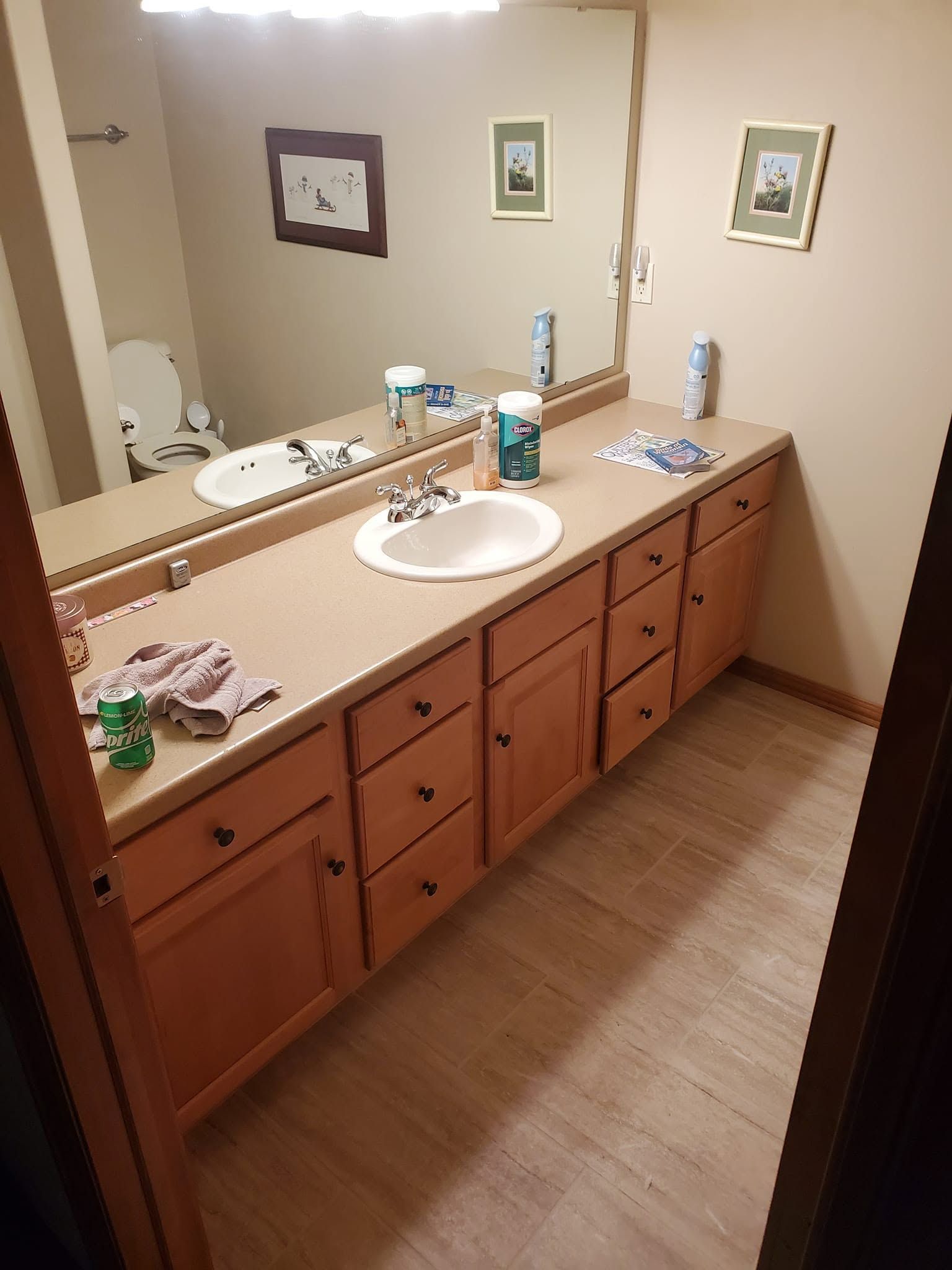 Bathroom vanity with double sinks, large mirror, and wooden cabinets on a tiled floor.