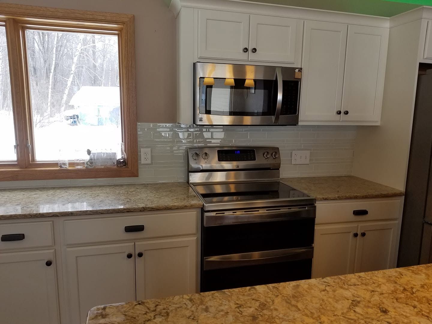 Kitchen with white cabinets, granite countertops, stainless steel stove and microwave, and a window over the sink.