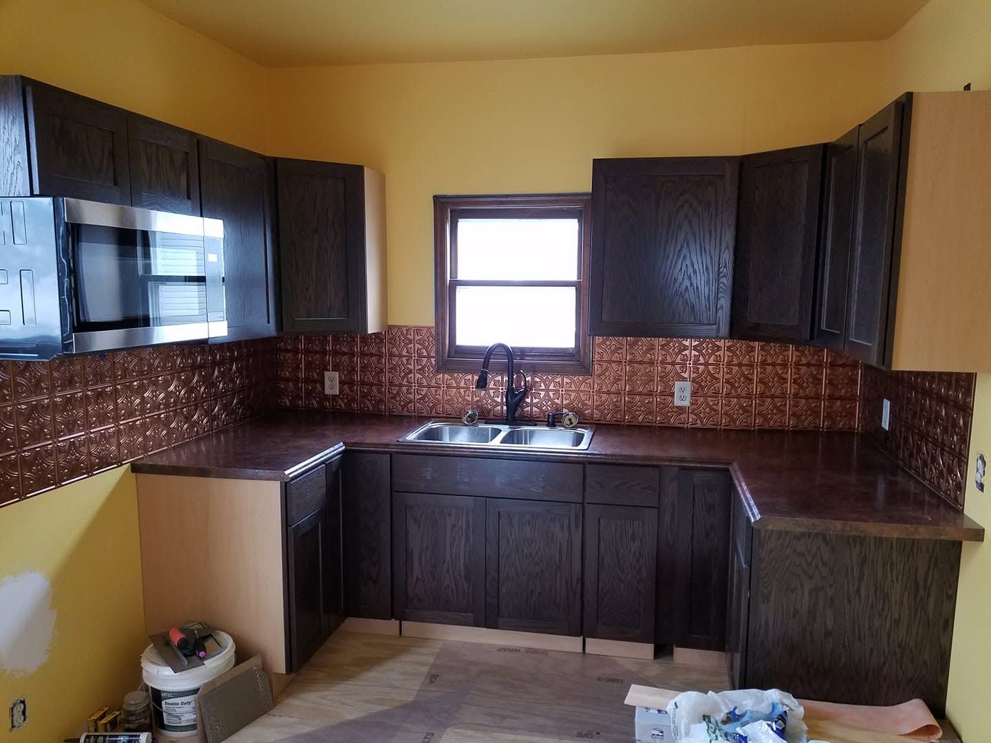 Small kitchen with dark wood cabinets, brown tile backsplash, and a window over the sink.