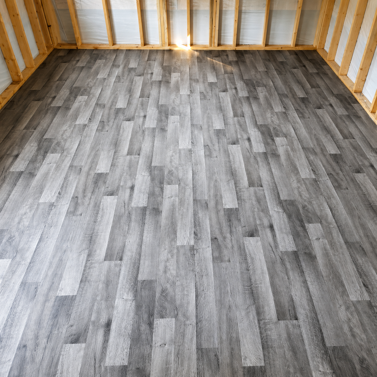 Empty unfinished room with gray wood-look flooring and exposed wall studs and insulation